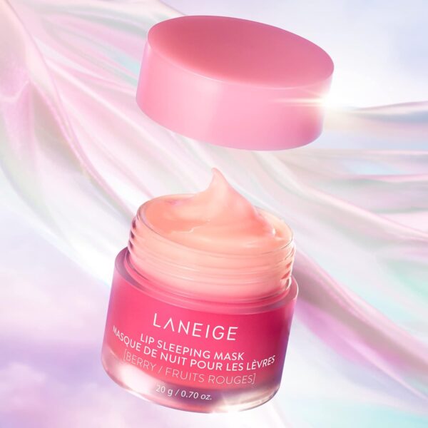 Alt text: A pink jar of LANEIGE Lip Sleeping Mask sits on a white surface, surrounded by fresh berries. The jar is open, revealing the creamy texture of the mask. The product promises to rejuvenate lips overnight, providing deep hydration and leaving them soft and supple.