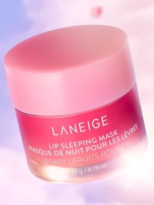 Alt text: A pink jar of LANEIGE Lip Sleeping Mask sits on a white surface, surrounded by fresh berries. The jar is open, revealing the creamy texture of the mask. The product promises to rejuvenate lips overnight, providing deep hydration and leaving them soft and supple.