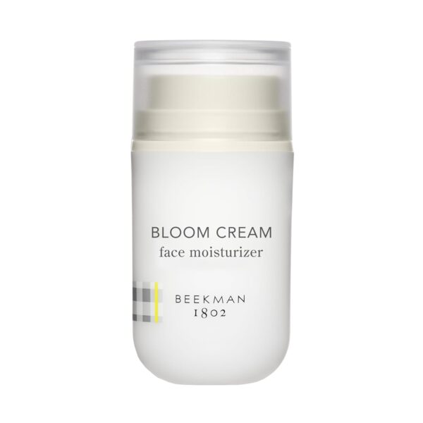 A white jar of "Beekman 1802 Bloom Cream Daily Face Moisturizer" with a minimalist label, set against a soft, pastel background.