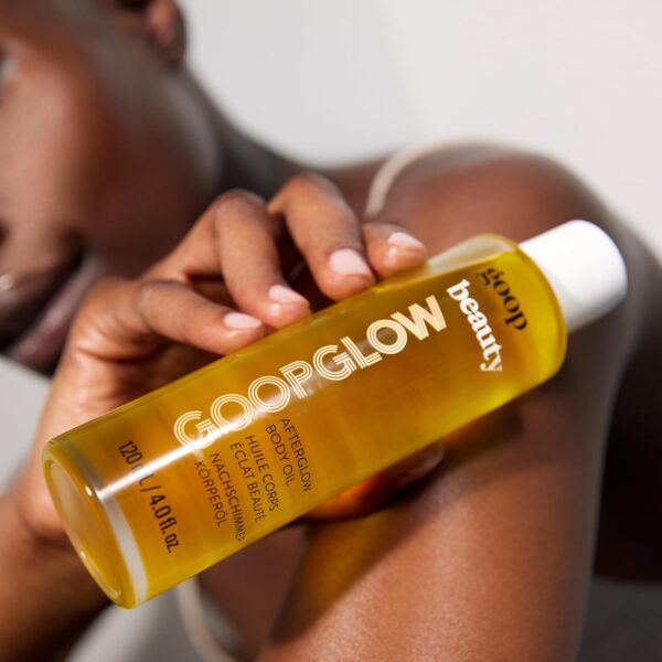 A bottle of goop Beauty Afterglow Body Oil displayed against a backdrop of soft, luxurious fabric. The bottle features a sleek design and clean branding, emphasizing the product's elegance and sophistication."