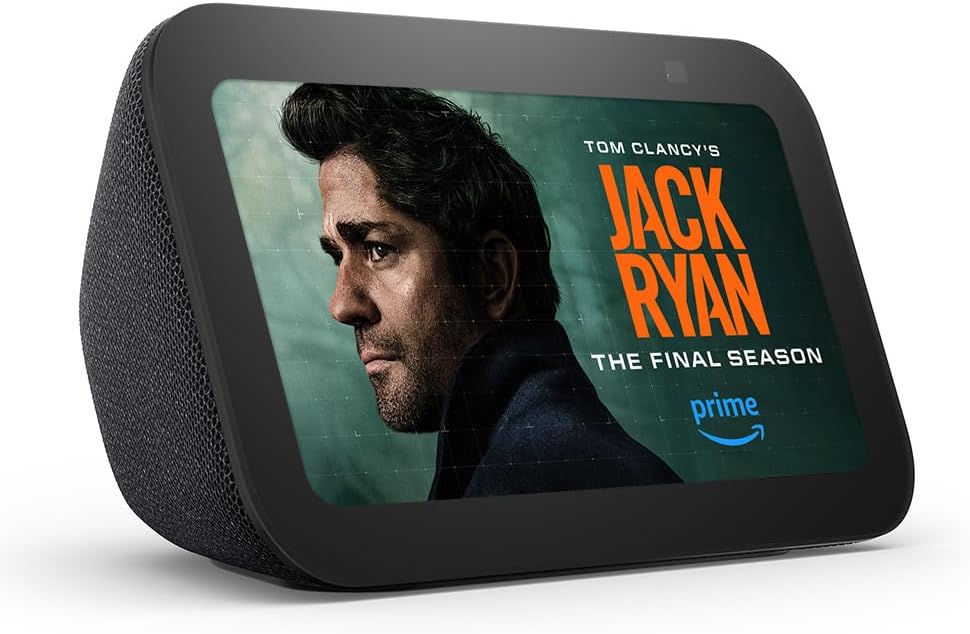 A compact smart display, the Echo Show 5 (3rd Gen, 2023 release), in a charcoal color. This updated version features twice the bass and improved clarity for a richer audio experience. The screen is designed for interactive touch-based control, with a front-facing camera for video calls and smart home integration. Its compact size is perfect for a bedside table or kitchen counter, providing visual and voice-activated access to weather updates, news, entertainment, and more.