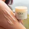 A luxurious spa-worthy exfoliator, the OSEA Undaria Cleansing Body Polish combines alpha hydroxy acid (AHA) with nourishing marine botanicals for rejuvenated skin. The bottle is surrounded by ocean-inspired imagery, conveying its natural ingredients and luxurious qualities.
